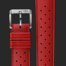 A close-up of a red textured watch strap with a silver-toned buckle, shown alongside a vertical detail view of the perforated strap pattern on a dark gray background.