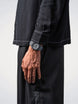 Person wearing a black shirt and pants with a watch on a plain background