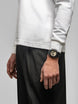 Person wearing a white long-sleeve shirt and black pants with a watch on a gray background
