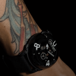 Black wristwatch with visible brand logo on a tattooed arm