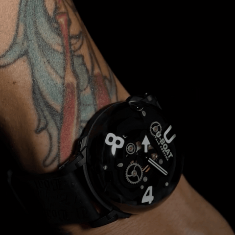 Black wristwatch with visible brand logo on a tattooed arm